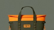 Olive green and bright orange YETI soft cooler bag with dual handles and side clips.