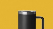 Black insulated travel mug with clear lid and stainless steel rim against a yellow background.