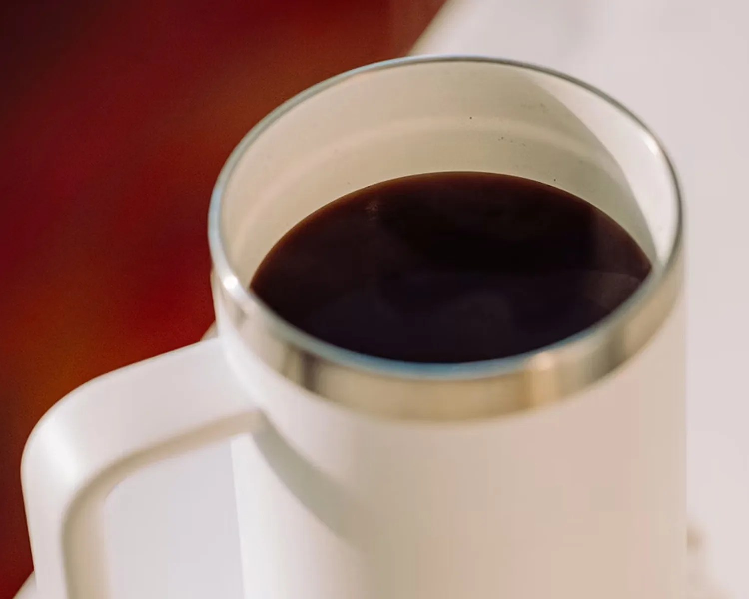 White ceramic coffee mug with a silver rim filled with black coffee.