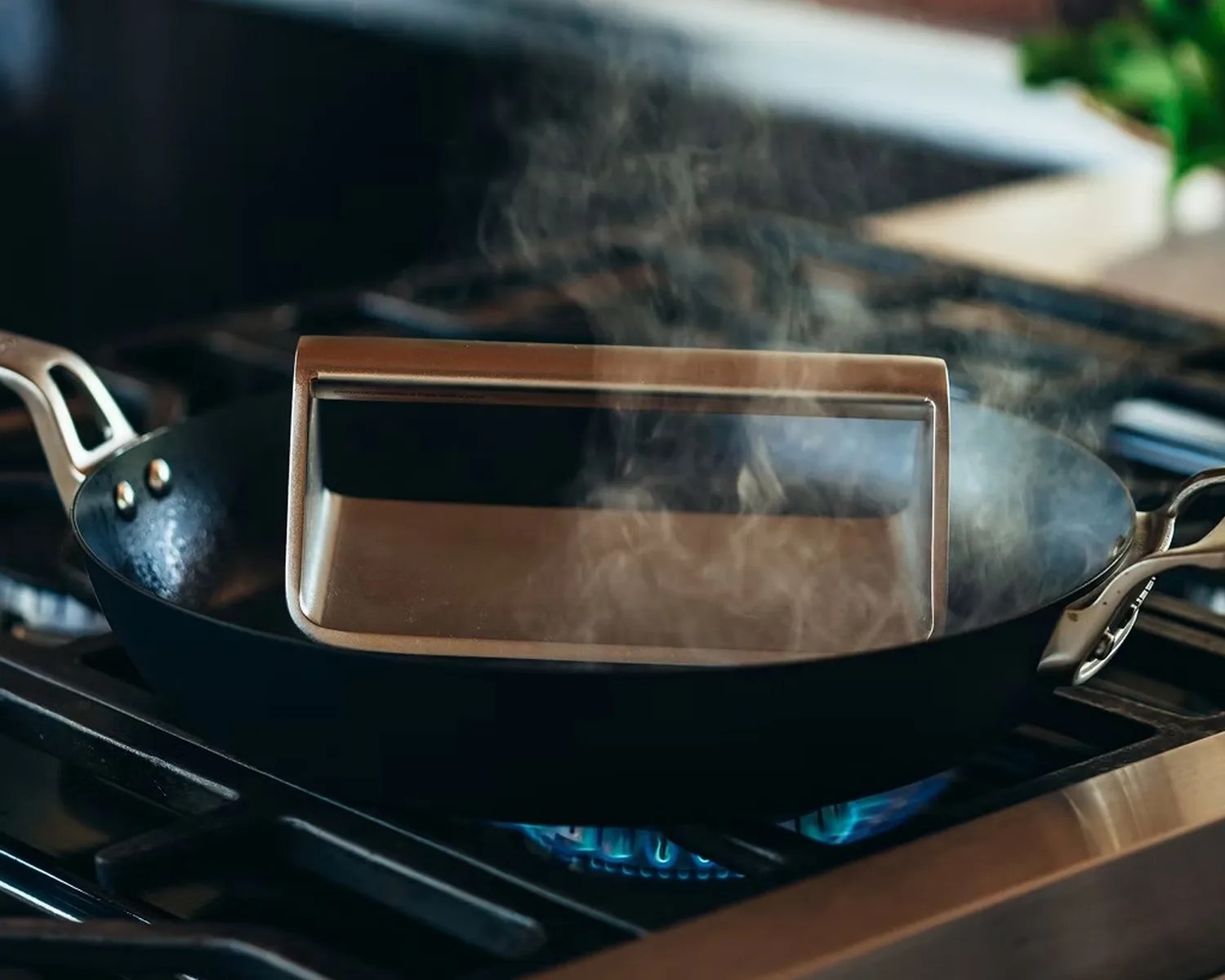 Black cast iron skillet on a gas stove with a metal press and steam rising.