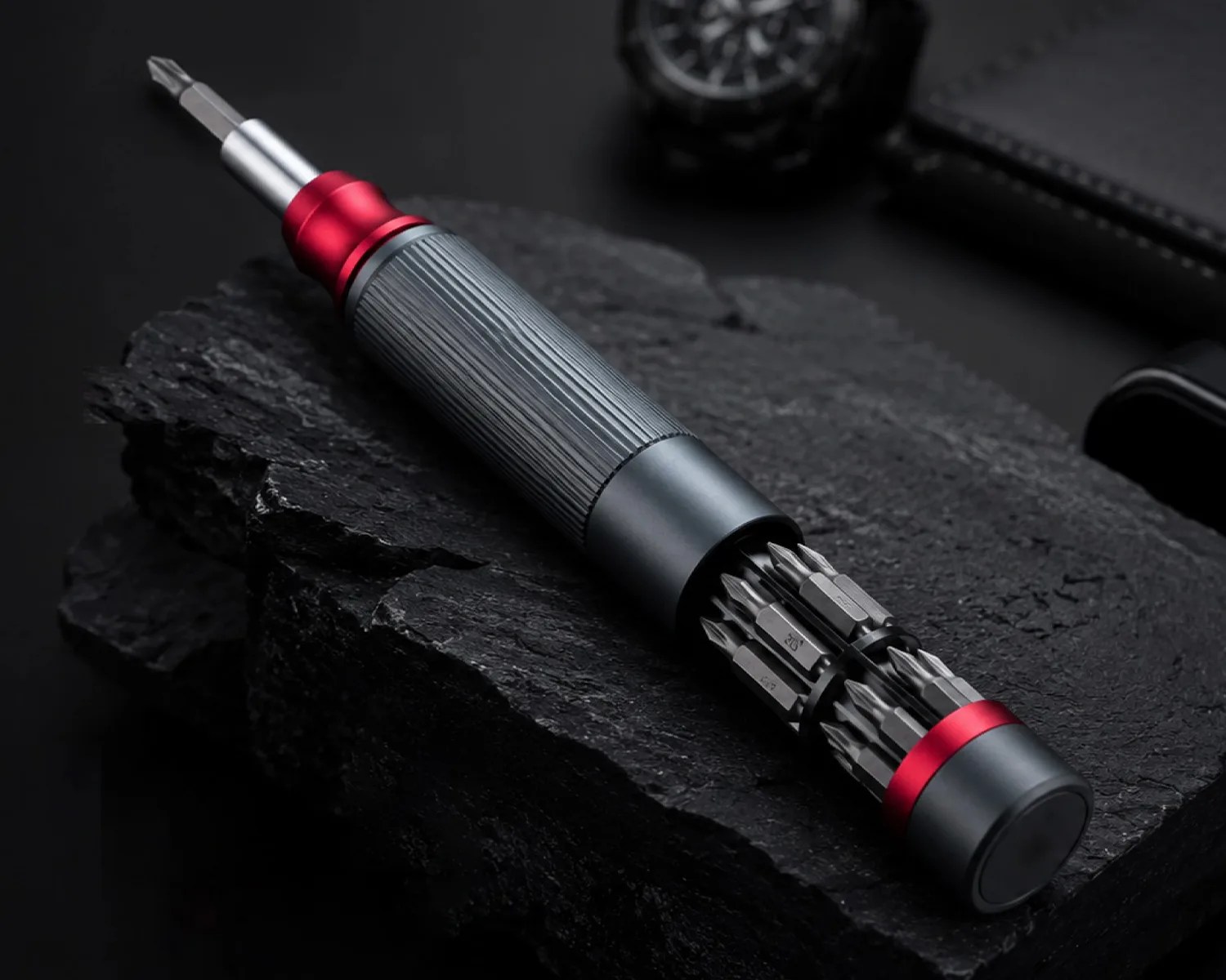 Metal screwdriver with a textured grip and multiple interchangeable bits stored in the handle, resting on black stone.