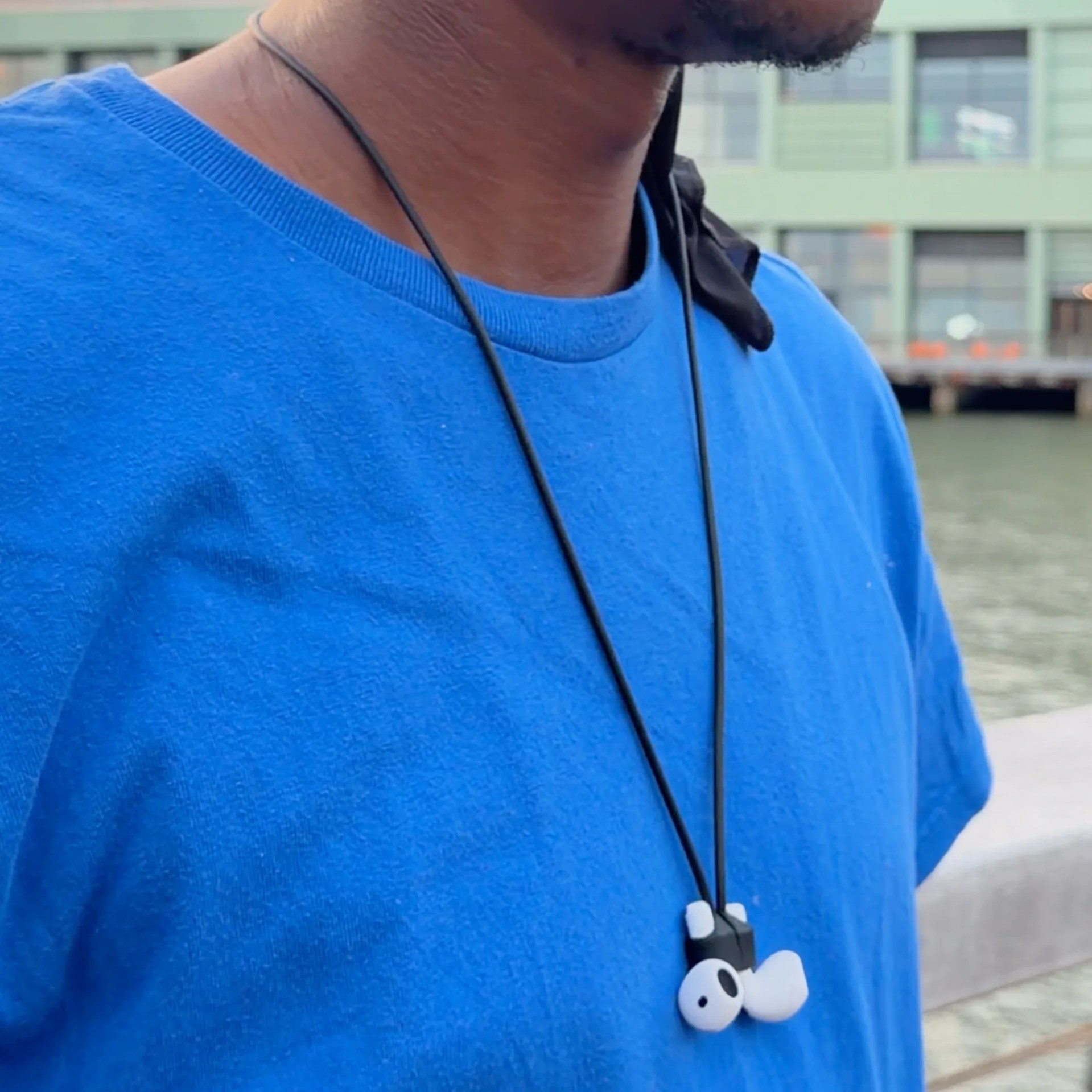 Black and white wireless earbuds hanging on a black cord worn around a person's neck with a blue shirt.