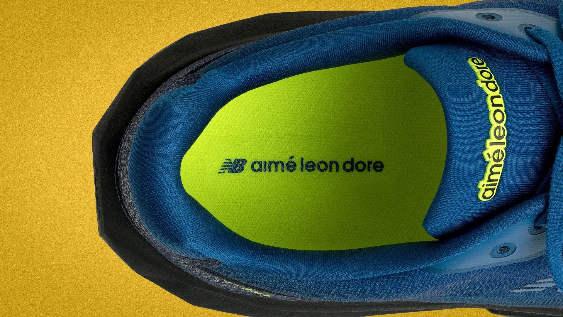 Top view of a blue sneaker with neon green insole featuring "aimé leon dore" and "NB" logos on a yellow background.