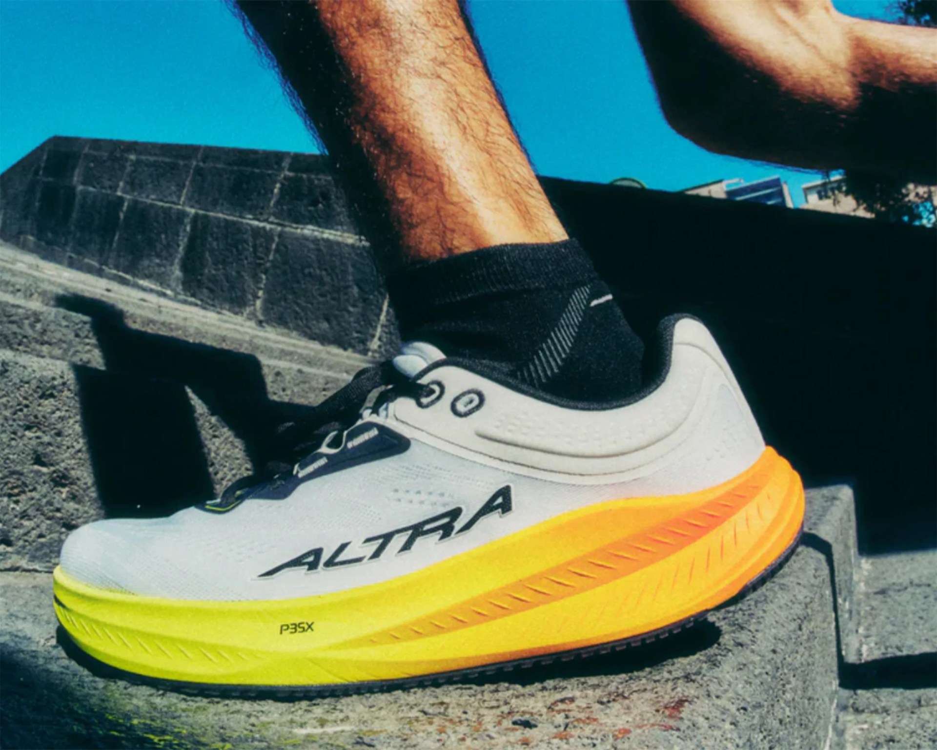 White and yellow Altra running shoe worn with black ankle sock on concrete steps.