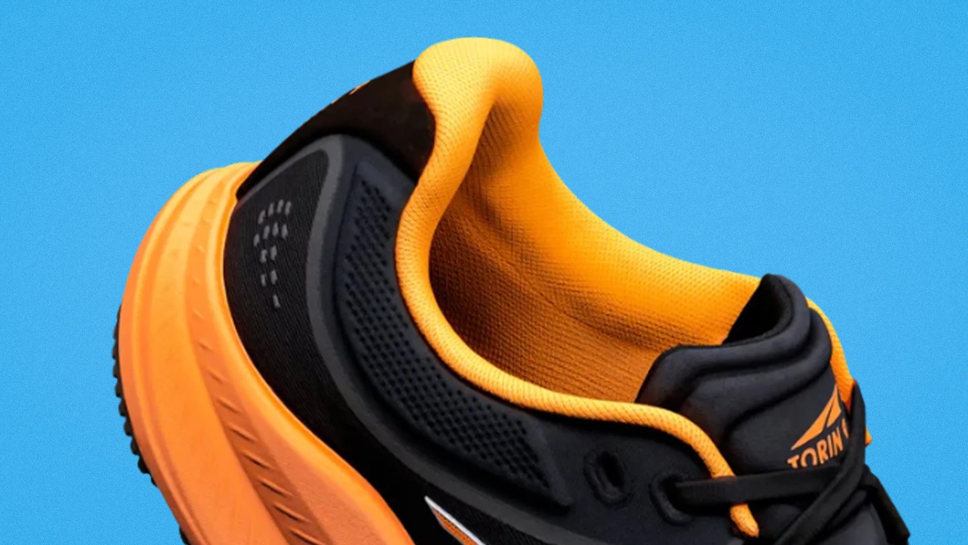 Black and orange athletic shoe with cushioned orange sole and padded orange collar against blue background.