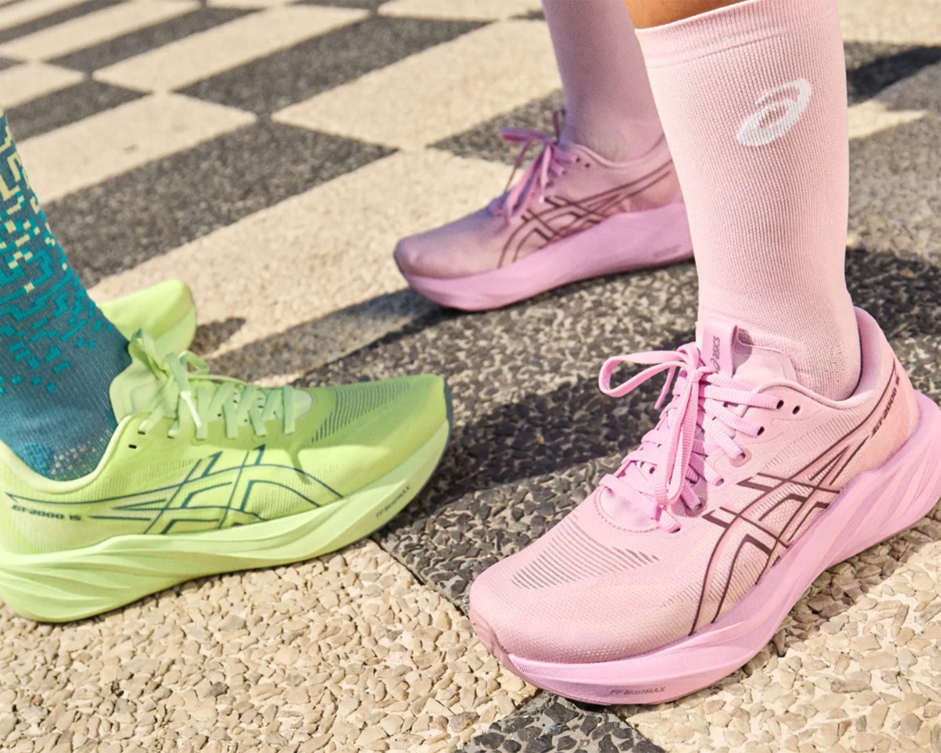 Pair of neon green and pink Asics running shoes on textured pavement.