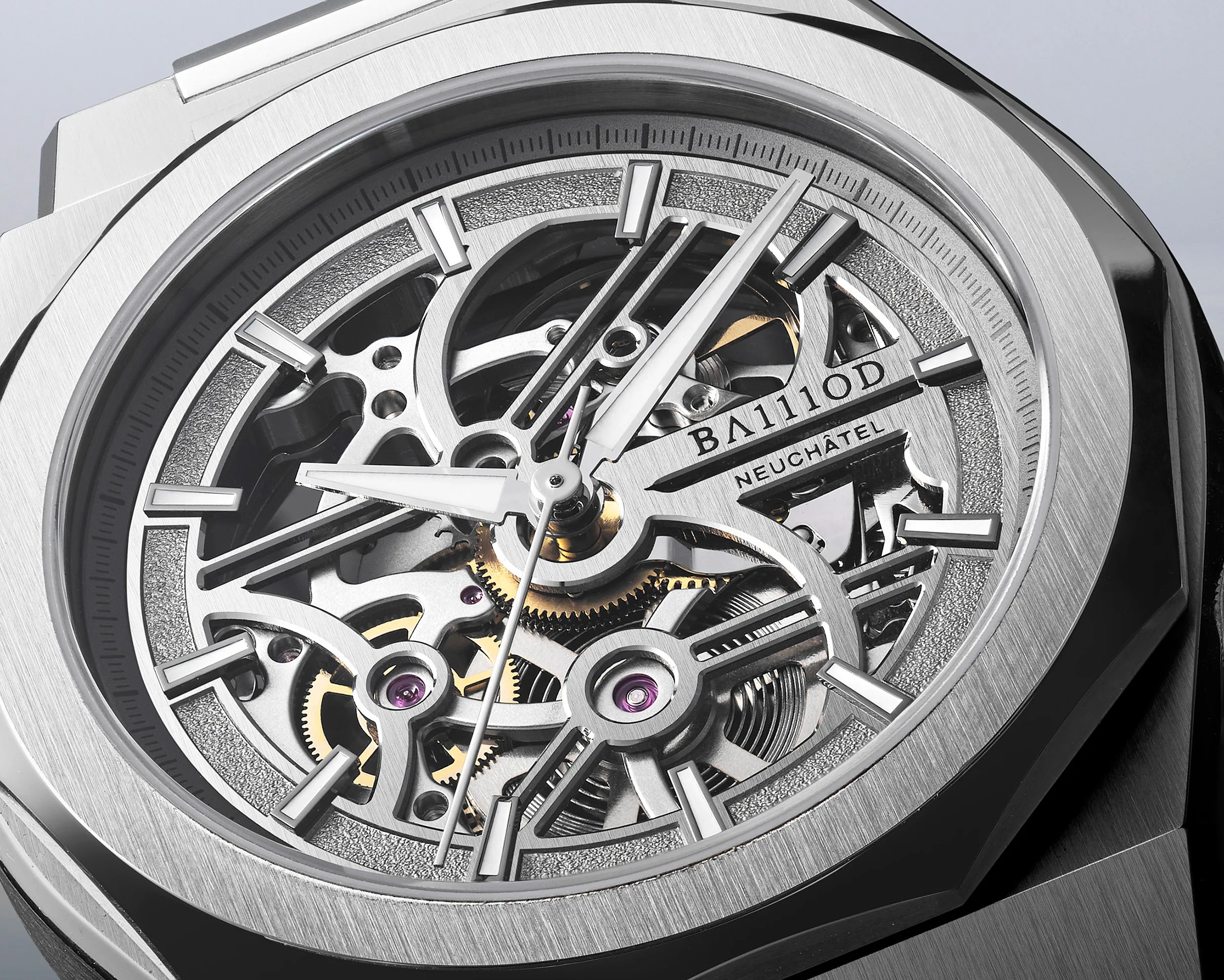 Close-up of a silver skeleton watch face with visible gears and "BA111OD NEUCH&Acirc;TEL" text on the dial.