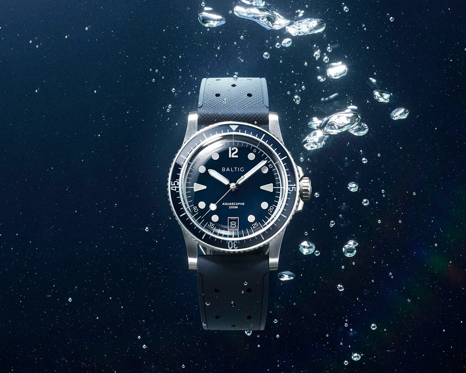 Diver-style wristwatch with a black dial, white markers, and a black perforated rubber strap submerged underwater with bubbles.