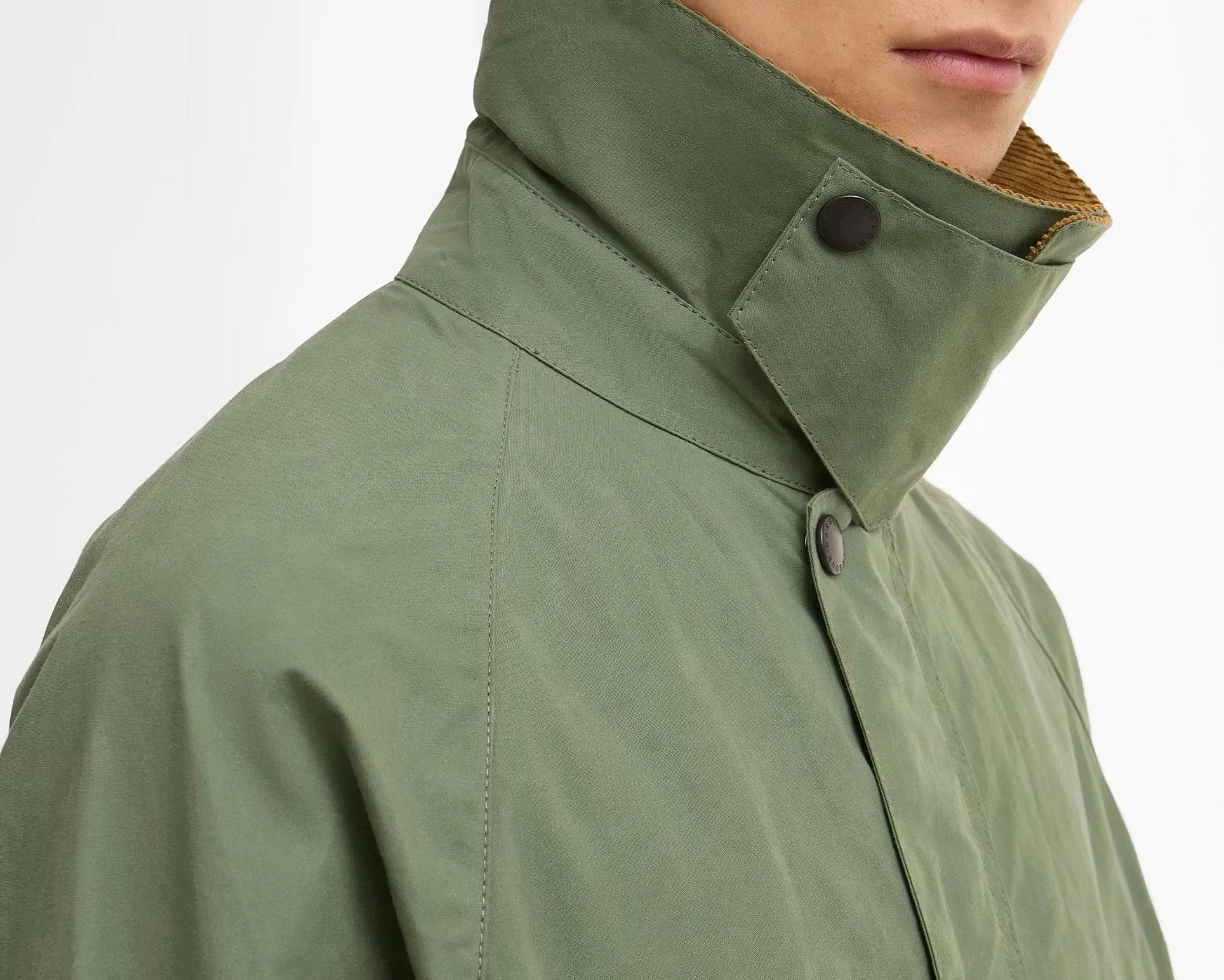 Olive green jacket collar with black snap buttons and brown corduroy lining worn by a person.