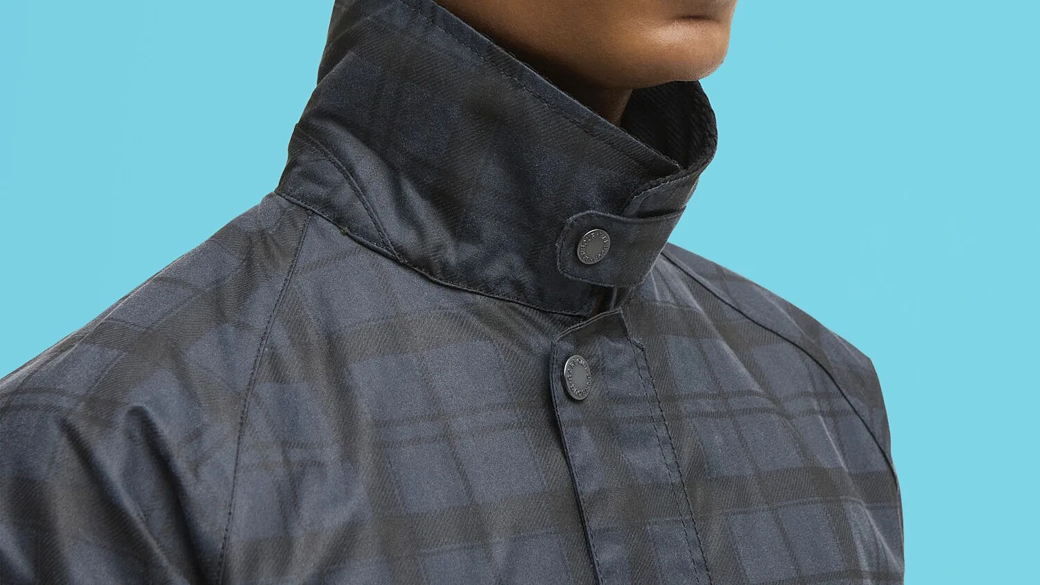Close-up of a dark gray plaid jacket collar with snap buttons against a light blue background.