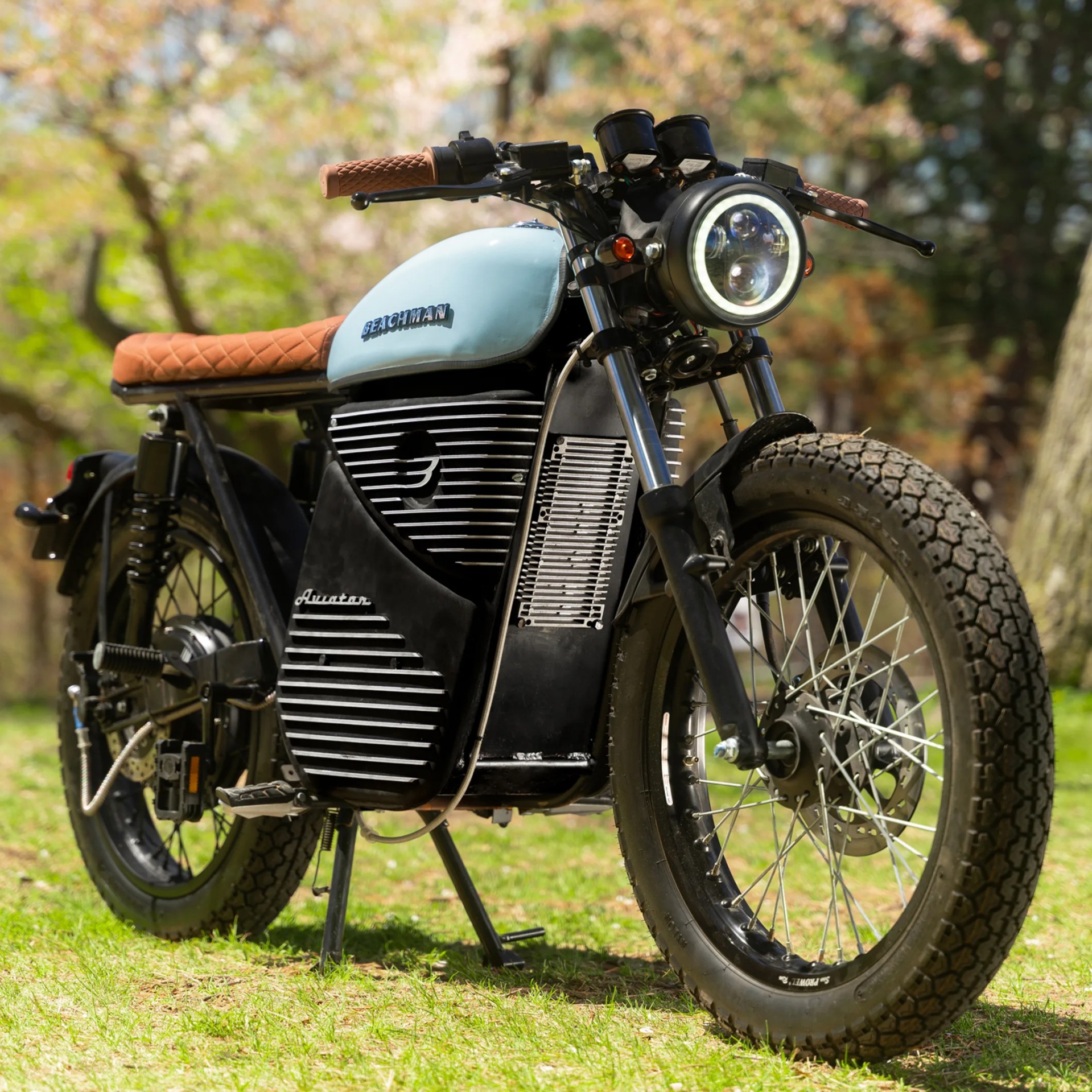 Light blue and black Beachman Aviator motorcycle with brown quilted seat and grips on grass.