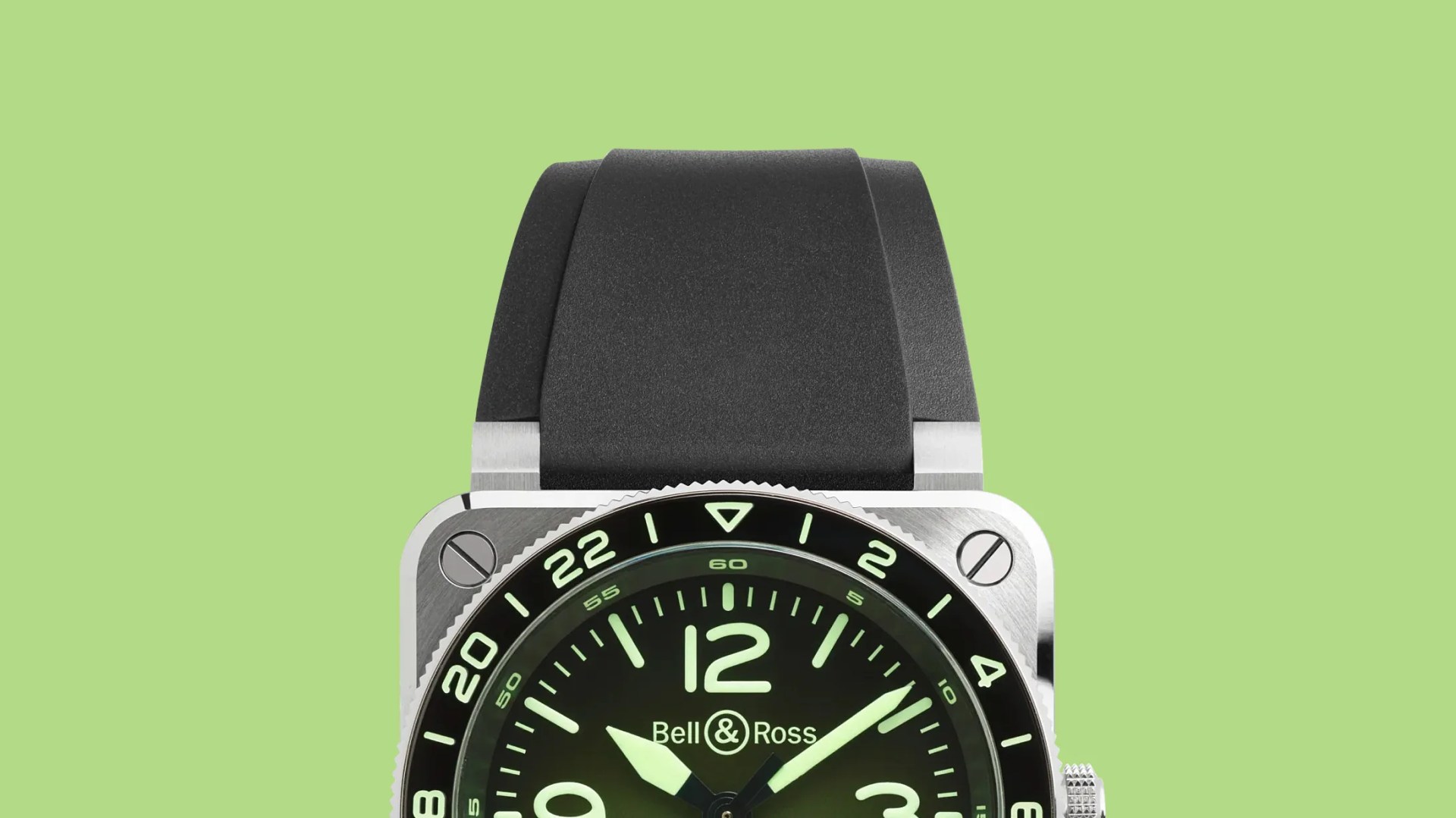 Square silver Bell & Ross watch with black bezel, green luminescent dial, and black rubber strap on green background.