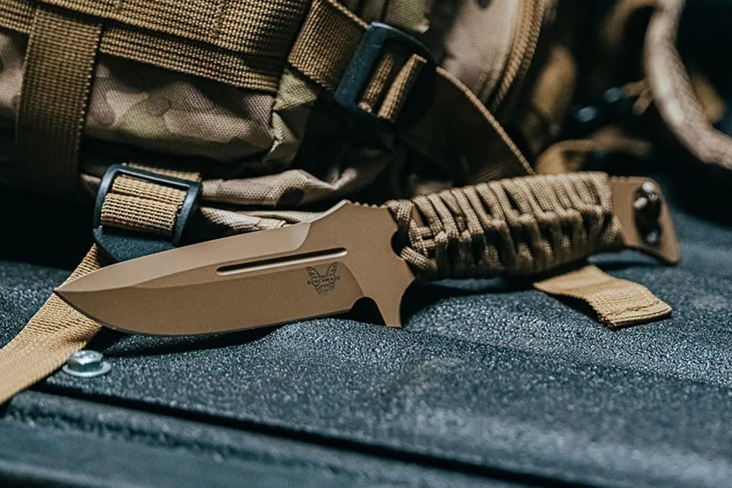Tactical fixed-blade knife with tan blade and paracord-wrapped handle resting on a textured surface.