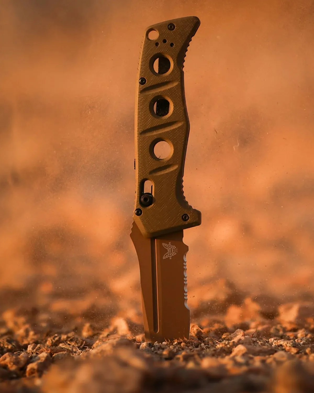 Tactical knife with a textured olive green handle and partially serrated blade stuck in rocky ground.