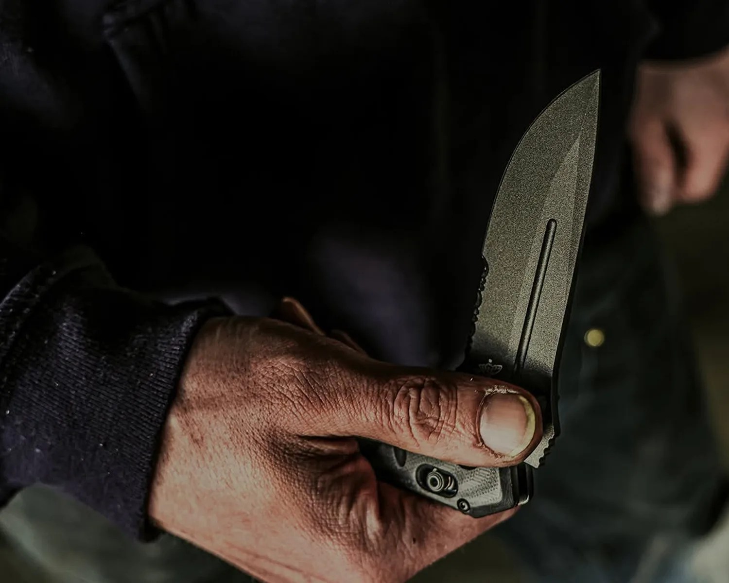 Hand holding a partially serrated folding knife with a textured black handle.