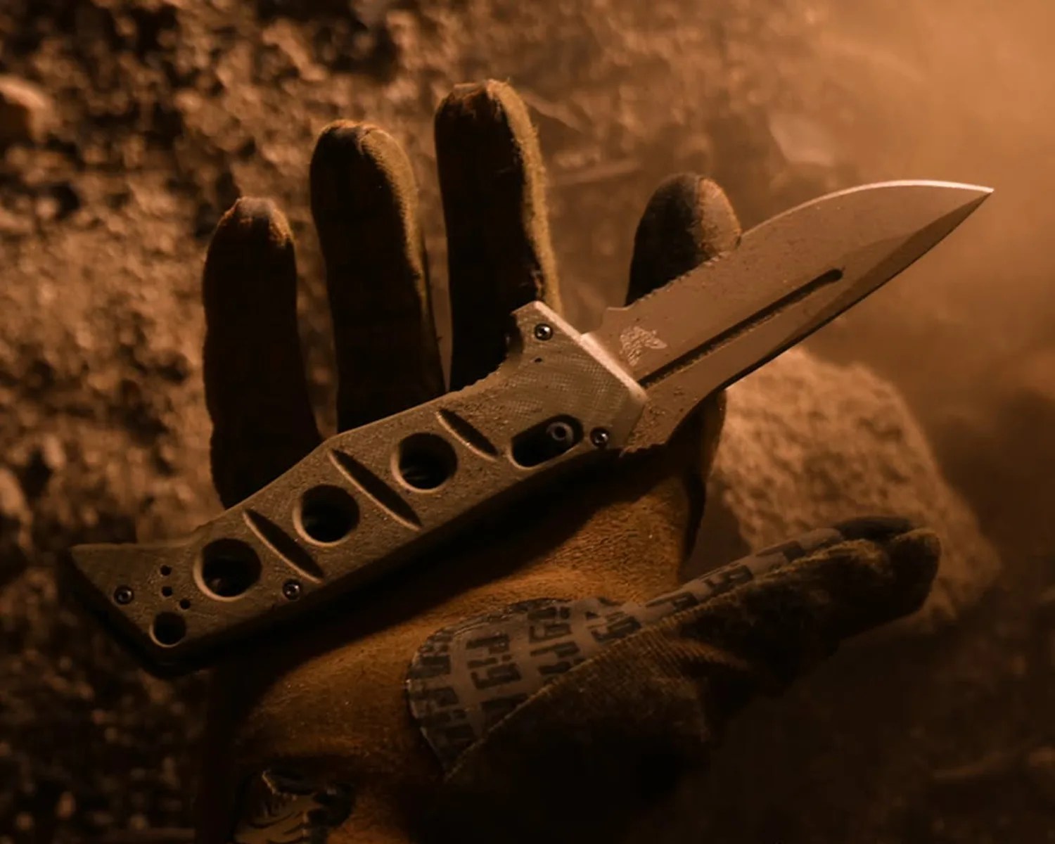 Tactical folding knife with a partially serrated blade and holes in the handle held in a gloved hand.