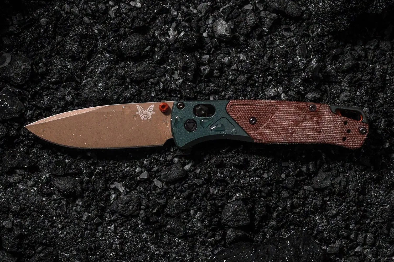 Benchmade folding knife with bronze blade, green and brown textured handle on black gravel.