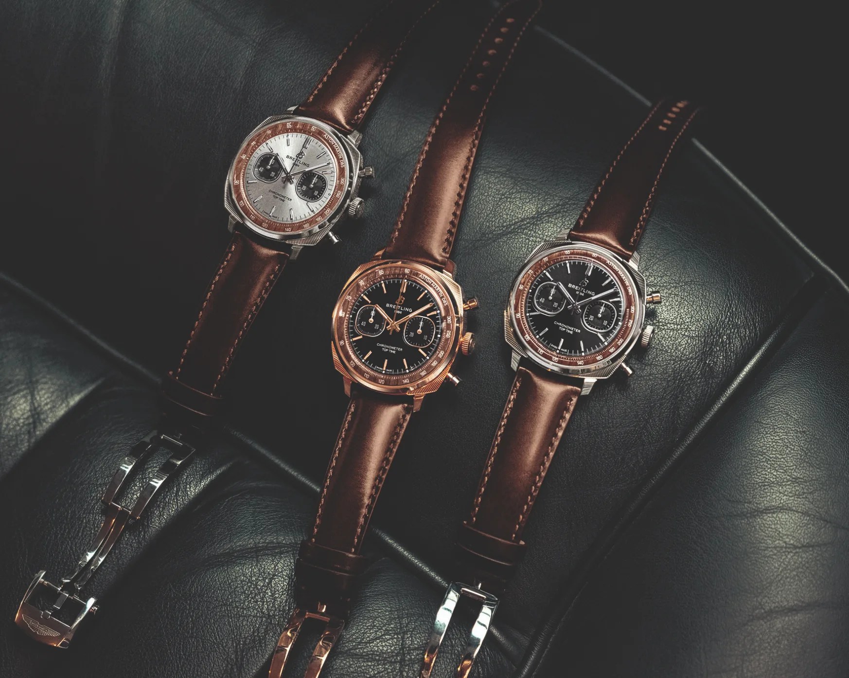 Three Breitling chronograph watches with brown leather straps on black leather surface.