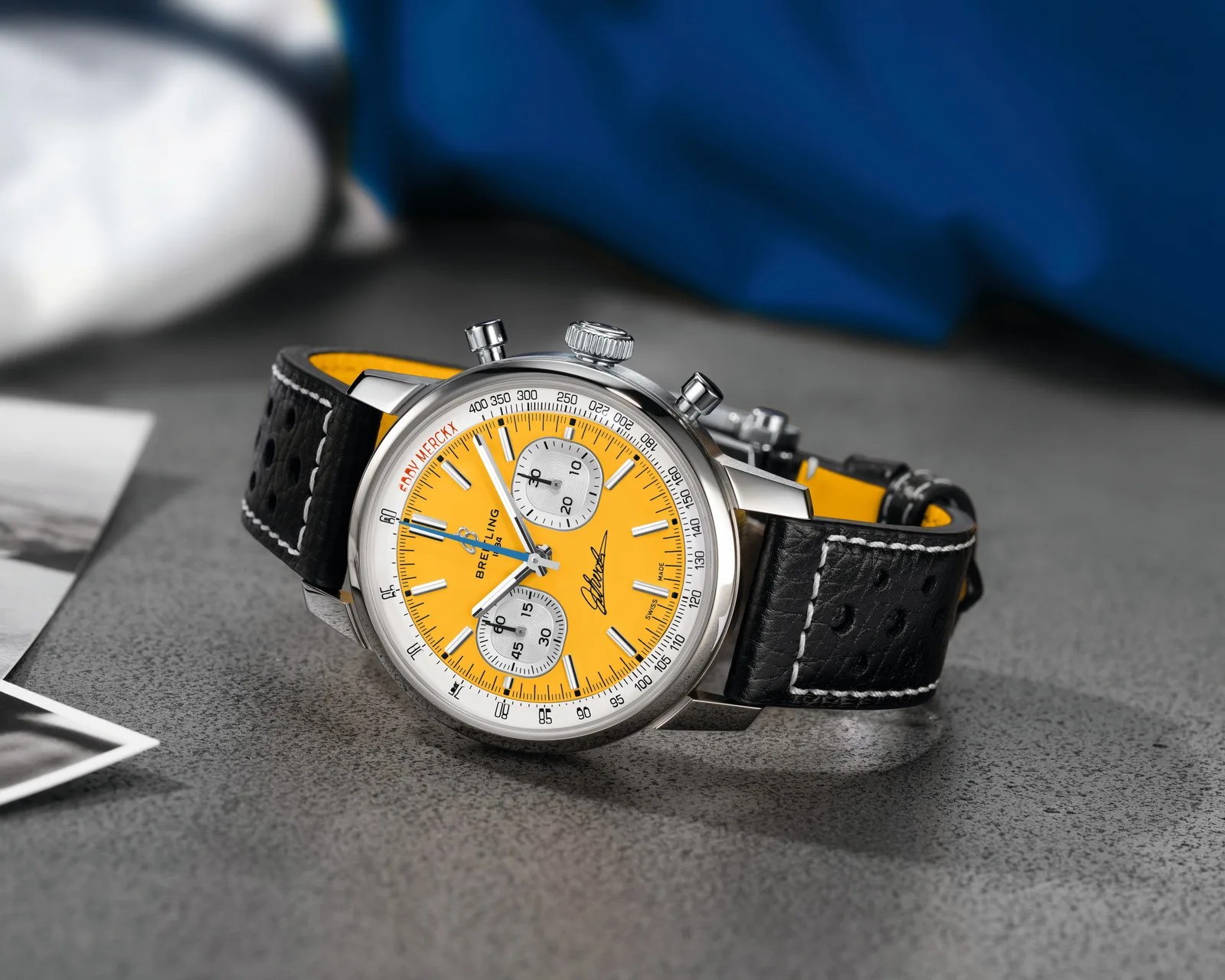 Breitling chronograph watch with yellow dial, silver subdials, and black perforated leather strap with white stitching.