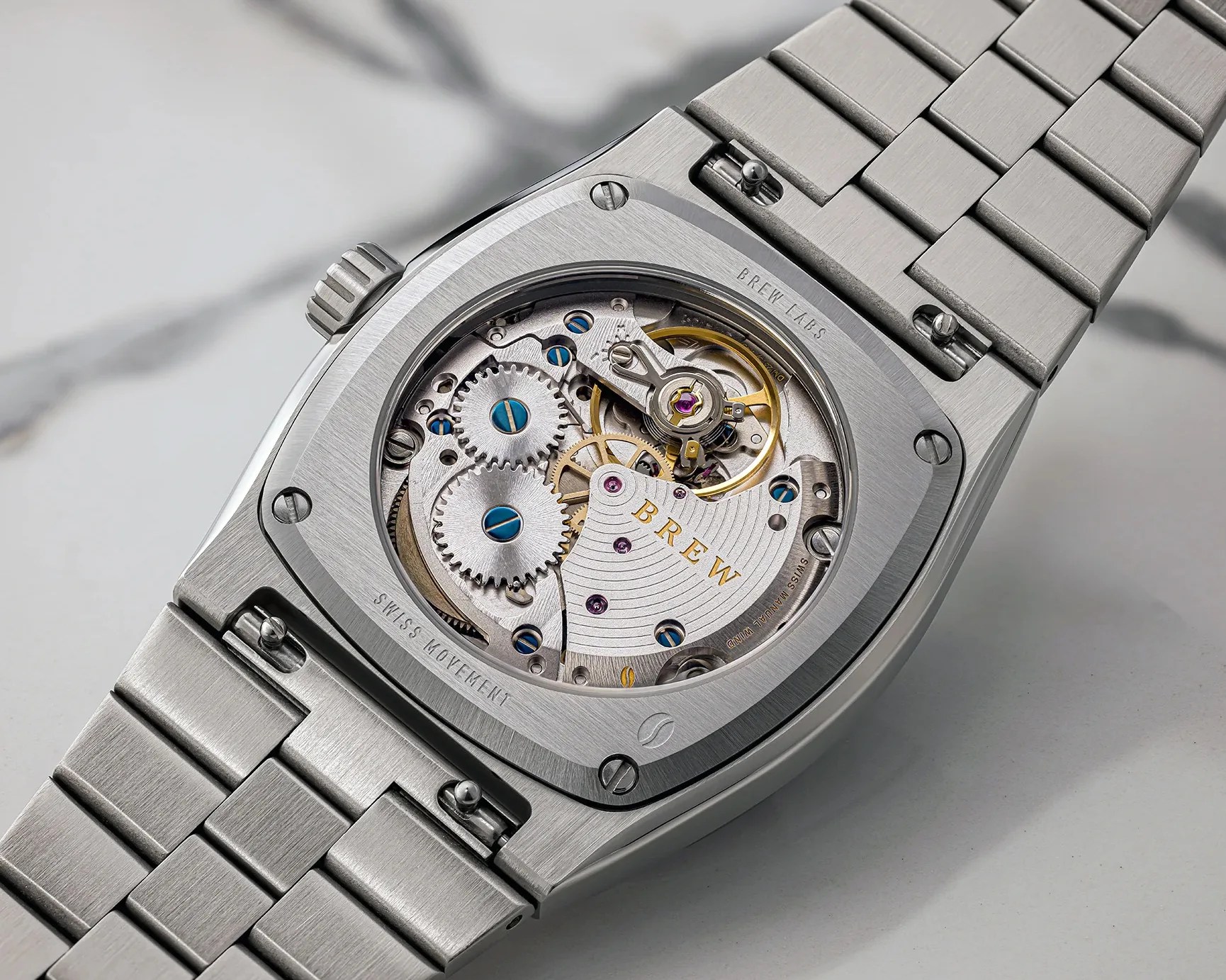 Close-up of a stainless steel wristwatch back showing visible mechanical movement with gears and screws.