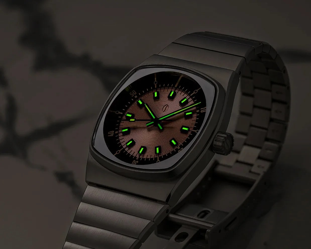 Black metal wristwatch with a brown textured dial and green luminescent hour markers and hands.