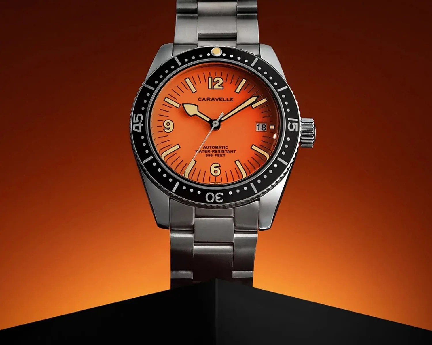 Stainless steel Caravelle wristwatch with bright orange dial and black rotating bezel on a black stand.