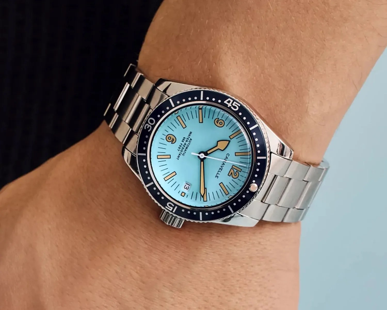 Silver metal wristwatch with a light blue dial and black bezel worn on a wrist.