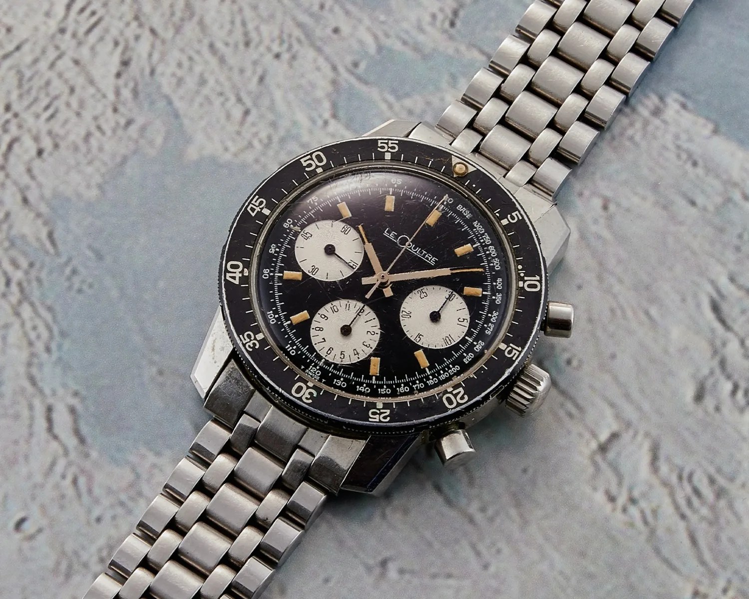 Vintage LeCoultre chronograph wristwatch with black dial, three white subdials, and stainless steel bracelet.