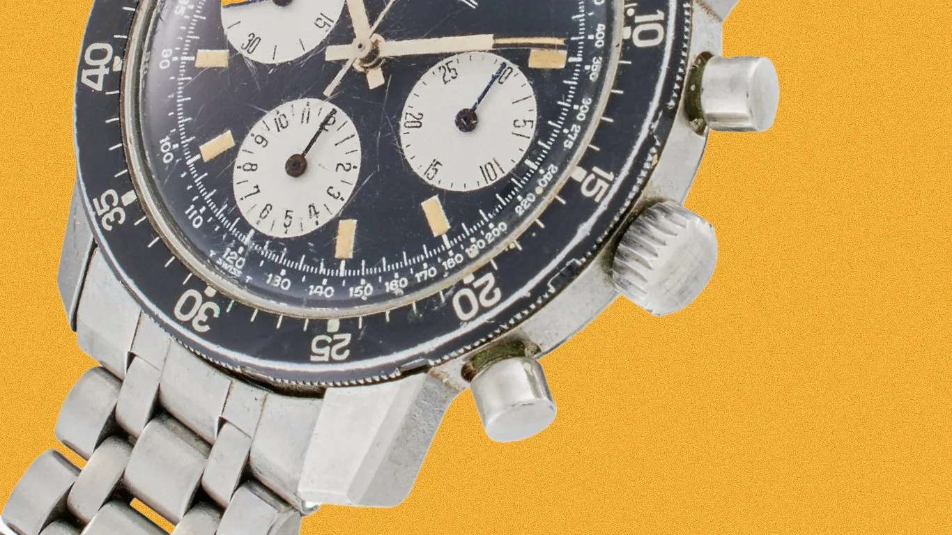 Close-up of a vintage stainless steel chronograph watch with a black bezel and three white subdials.
