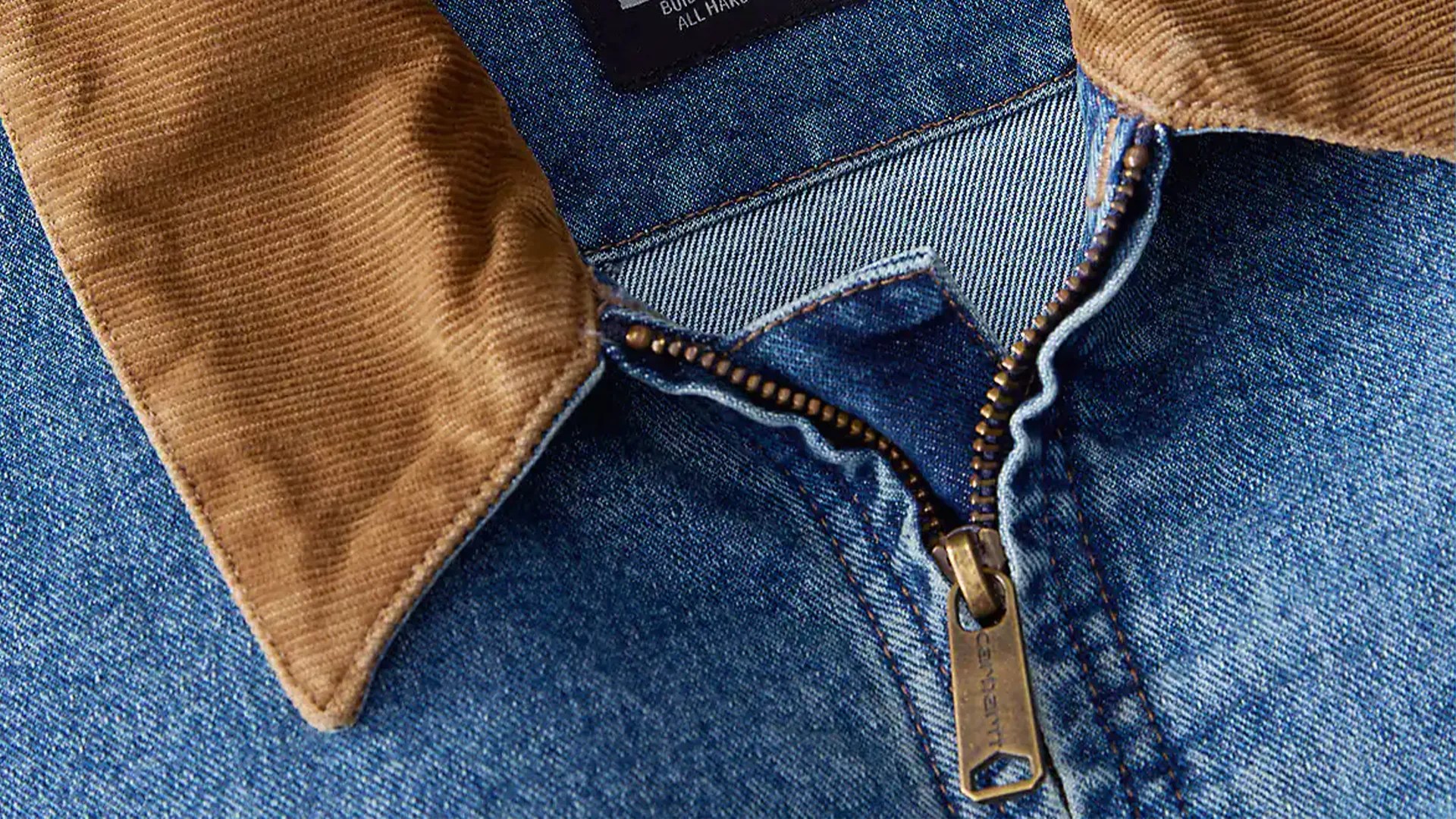 Close-up of a blue denim jacket with a partially unzipped brass zipper and a brown corduroy collar.