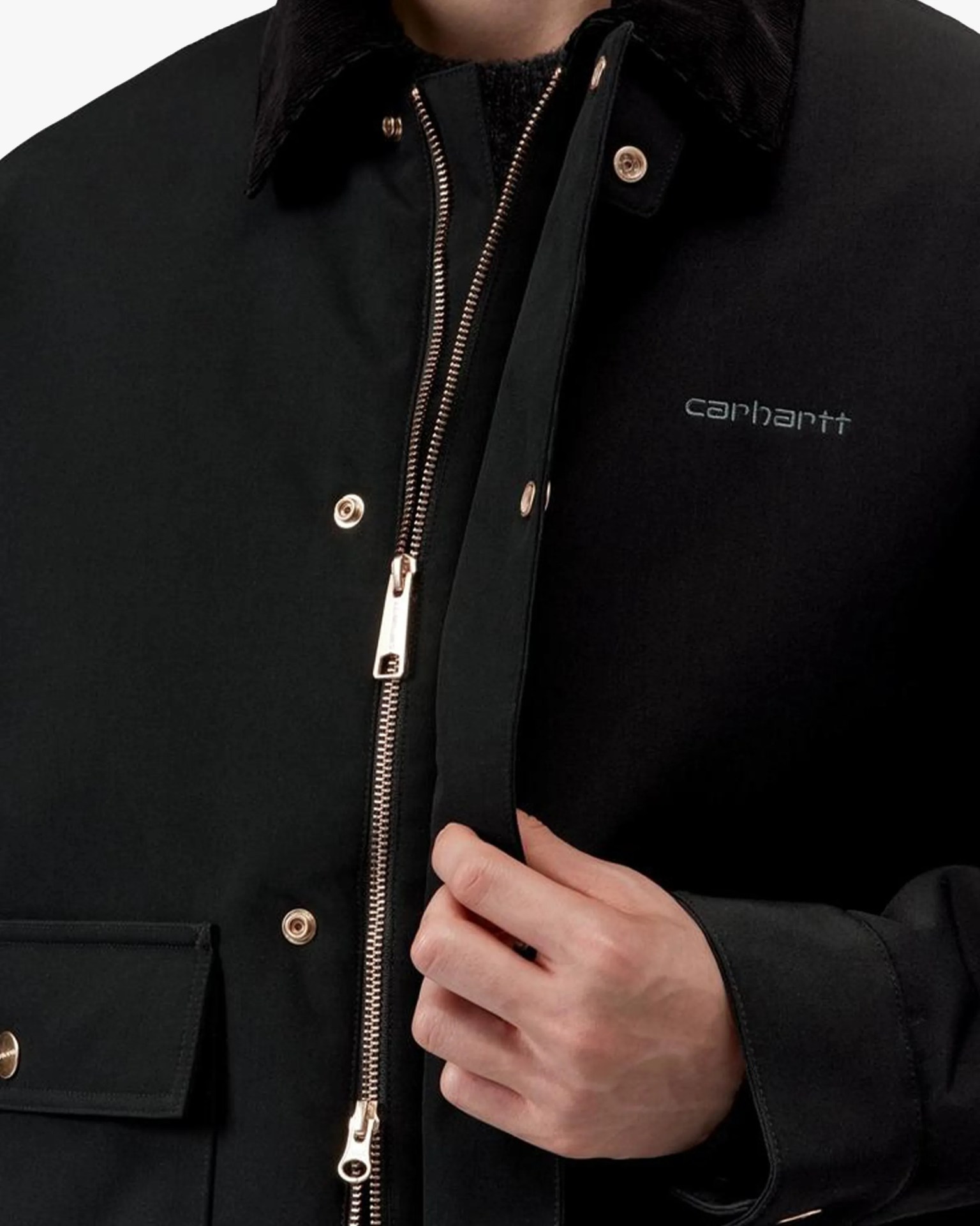 Close-up of a black Carhartt jacket with a metal zipper and snap buttons, held by a hand.