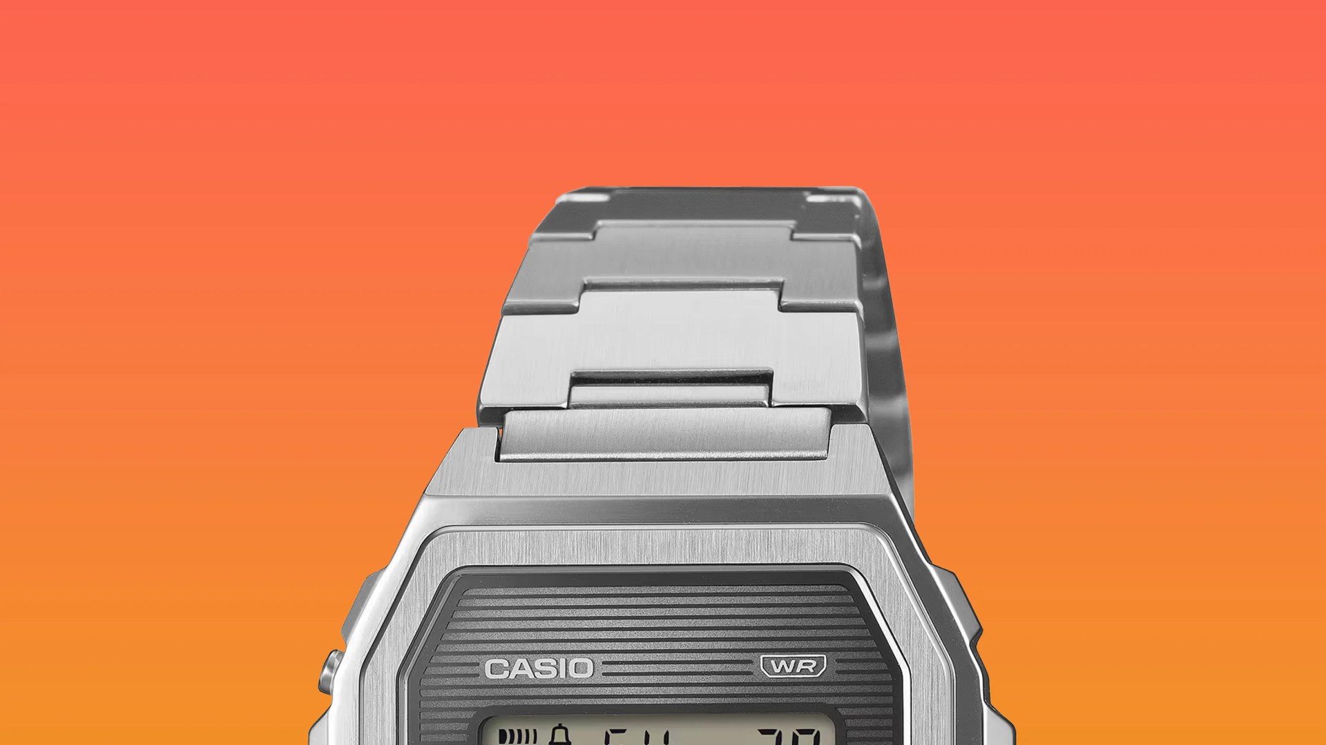Silver metal Casio digital watch with a stainless steel link bracelet on an orange gradient background.