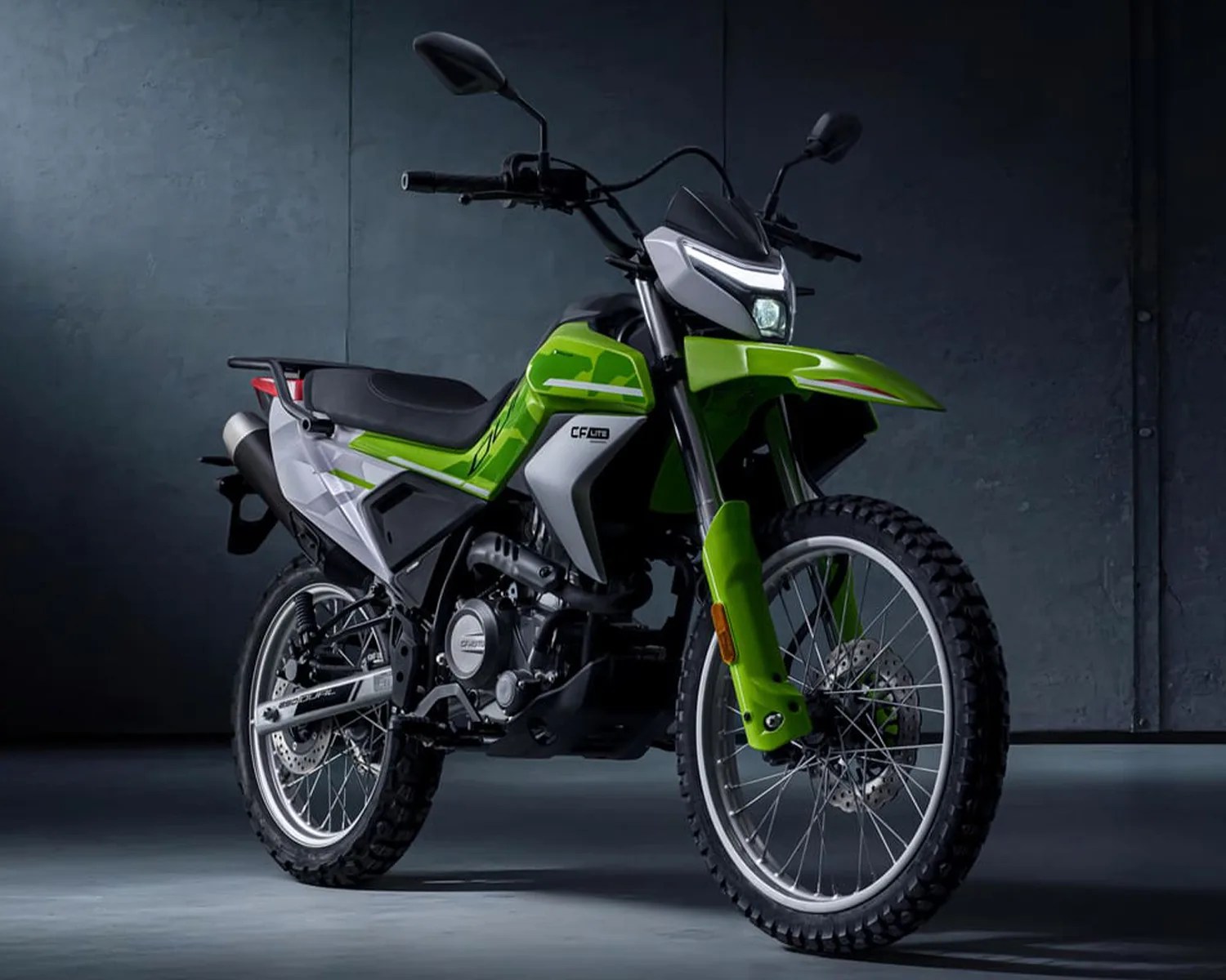 Green and white CF Moto off-road motorcycle with knobby tires in a dark studio.