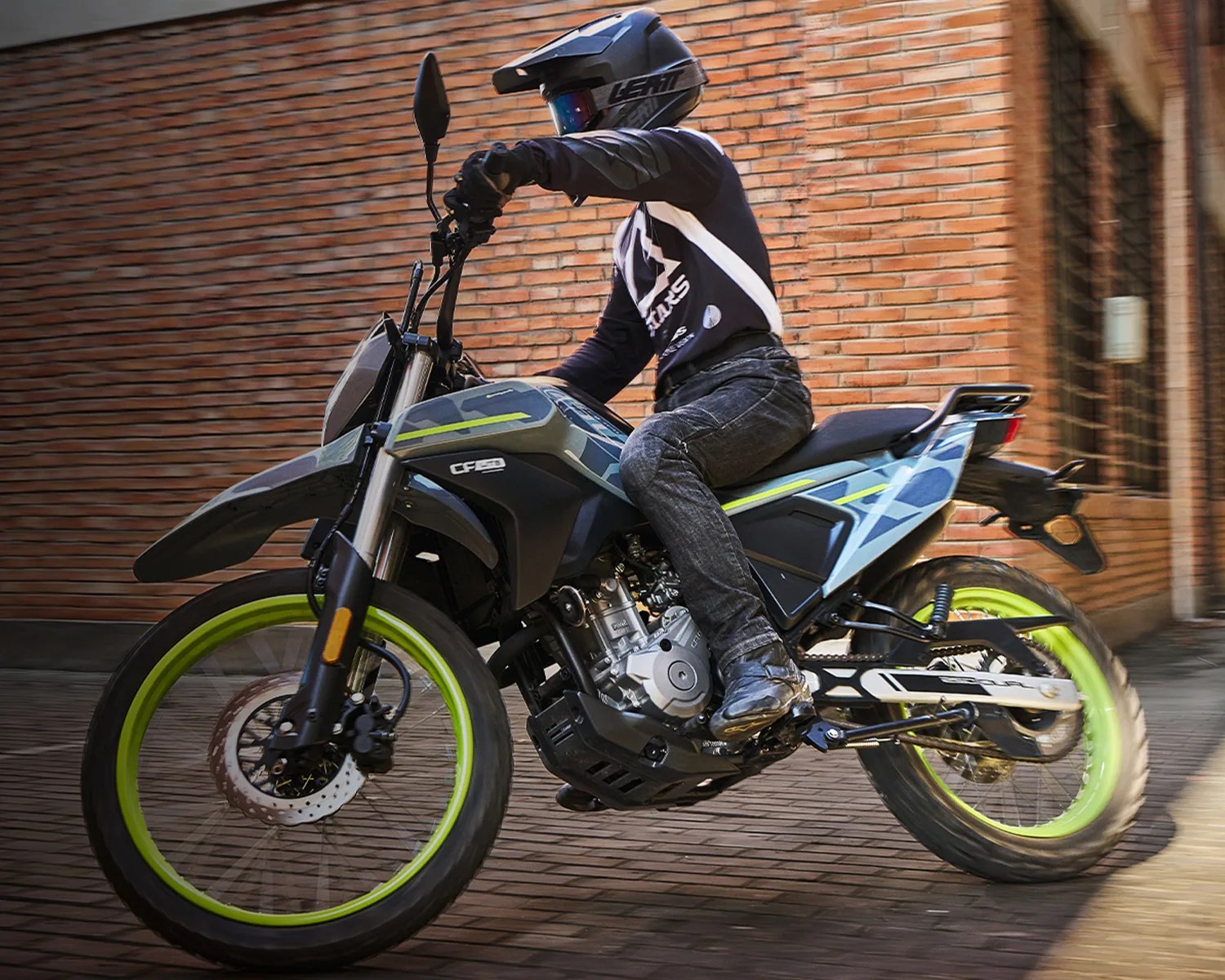 Black and gray CF Moto motorcycle with neon yellow wheel rims ridden on a brick street.