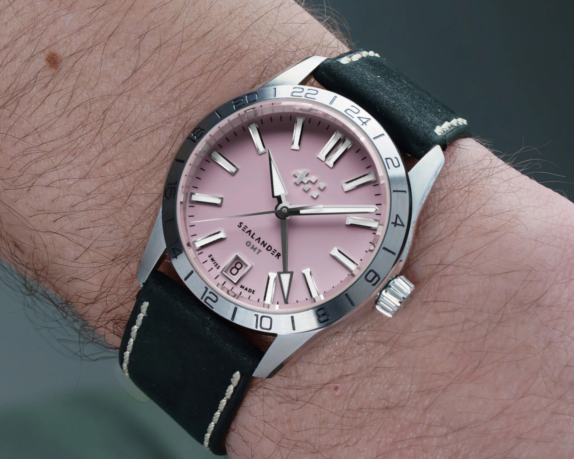 Wristwatch with pink dial, silver bezel marked 1-24, and black leather strap with white stitching.