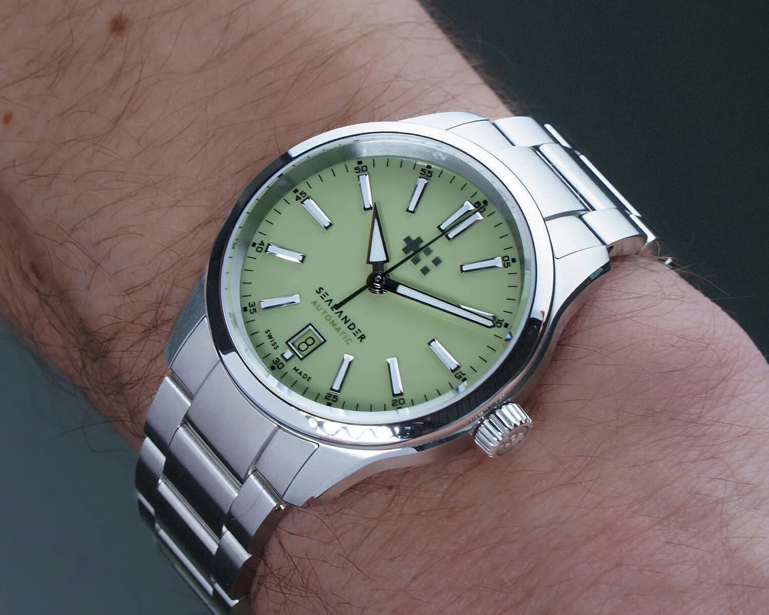 Silver metal wristwatch with a pale green dial, rectangular hour markers, and date window at 6 o'clock.
