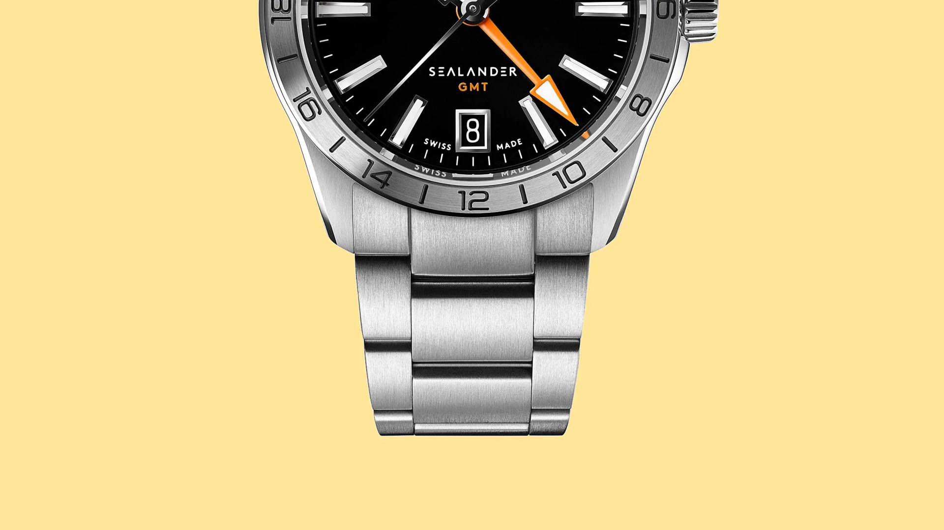 Close-up of a silver stainless steel wristwatch with a black dial, orange GMT hand, and date window on a yellow background.