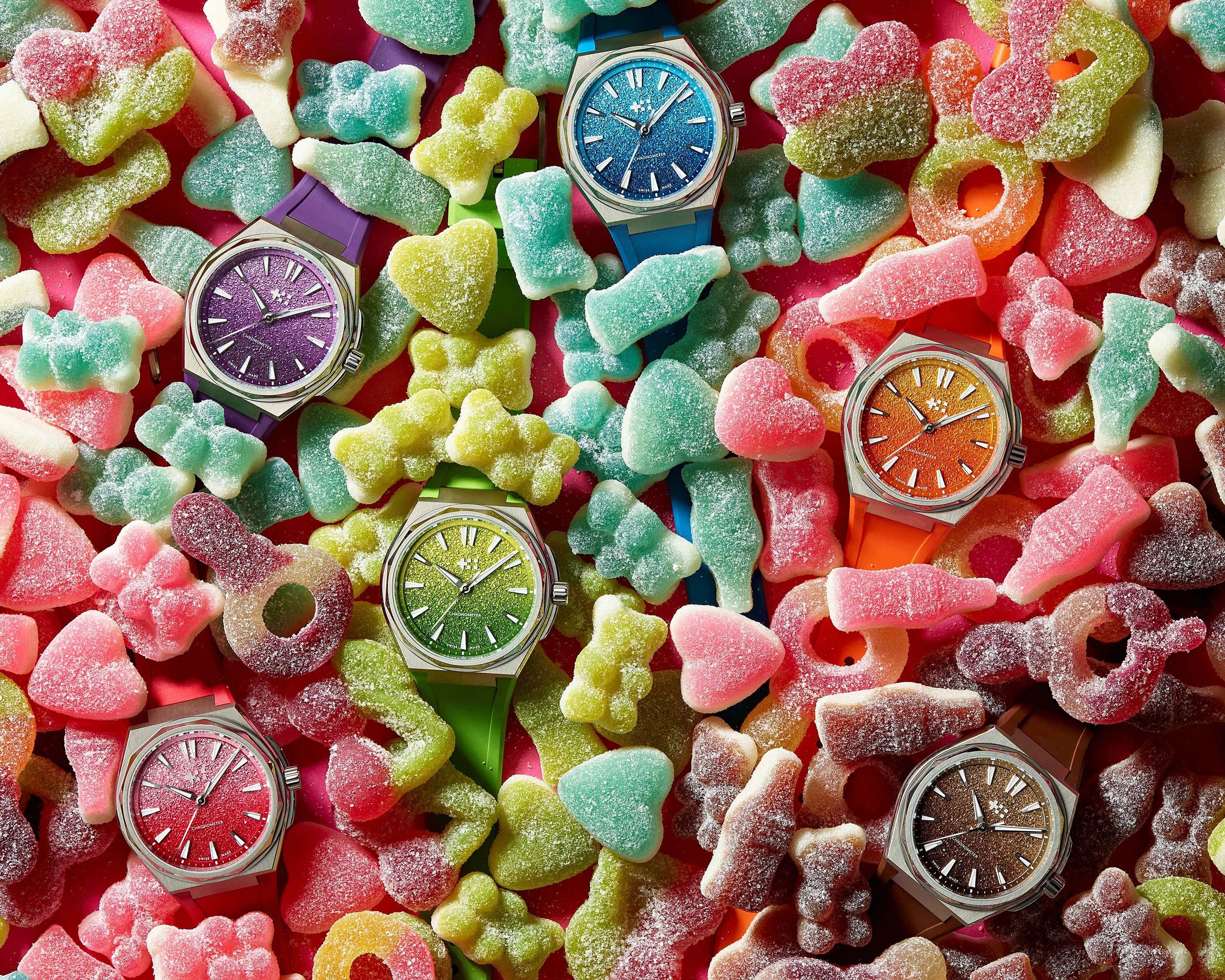 Six colorful wristwatches with textured dials and matching straps placed among assorted sugar-coated gummy candies.
