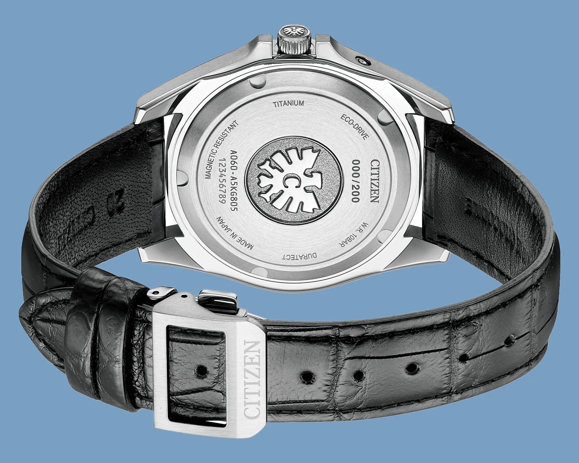 Back of a Citizen titanium Eco-Drive watch with black leather strap and silver buckle on blue background.
