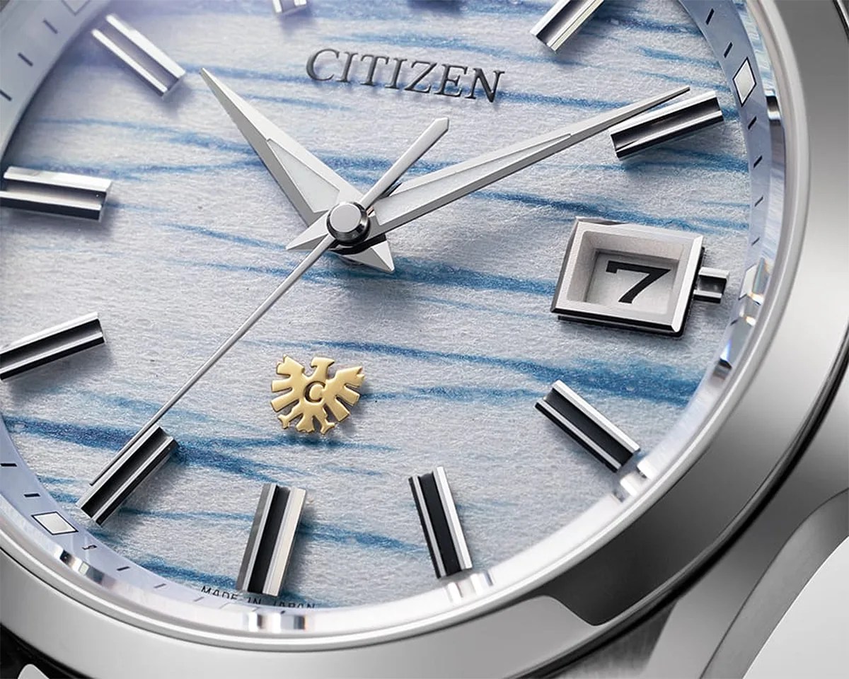 Close-up of a Citizen watch face with silver hands, black and silver hour markers, a date window showing "7," and a textured blue and white dial.