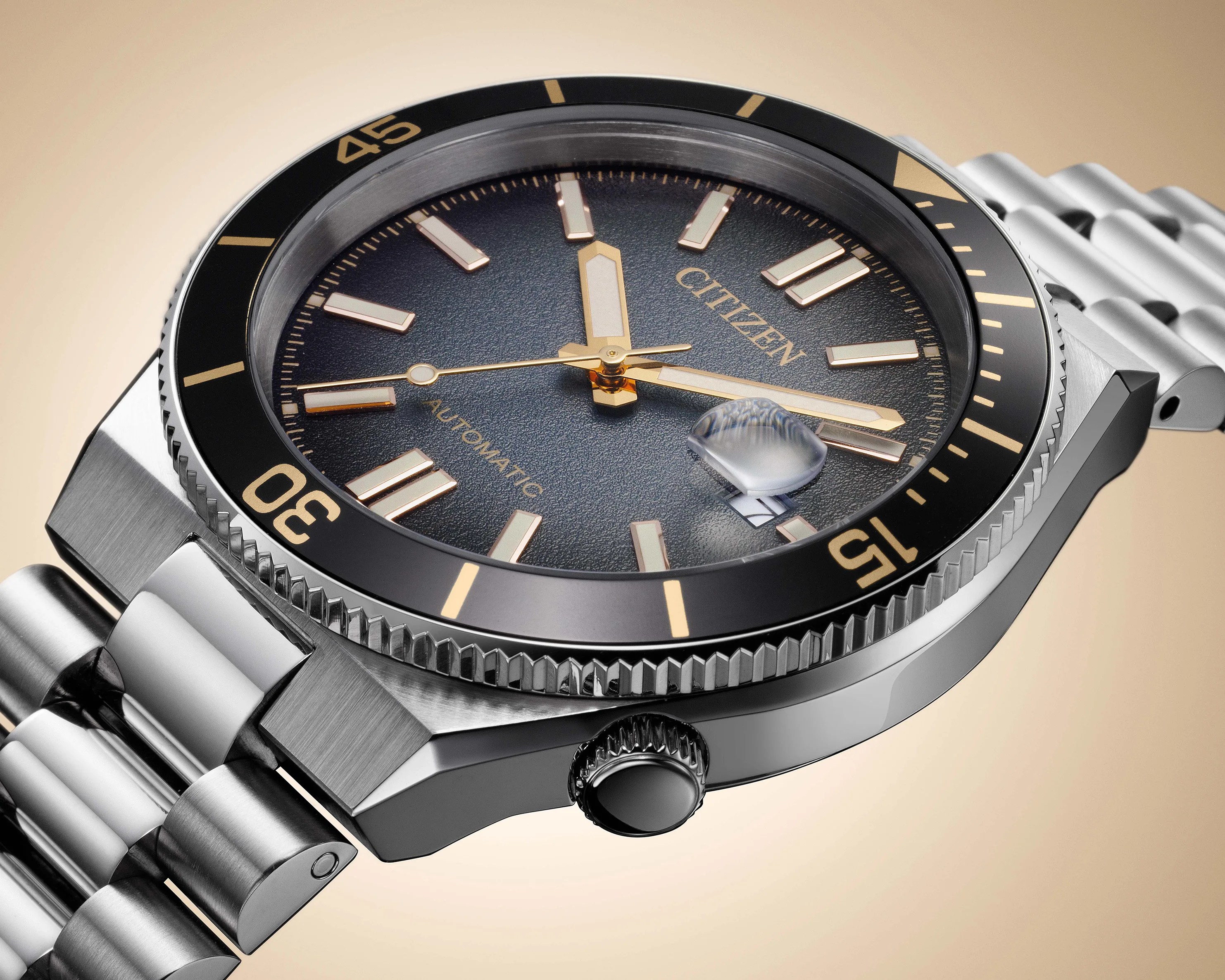 Close-up of a Citizen automatic watch with a black textured dial, gold-tone markers and hands, black bezel, and stainless steel bracelet.