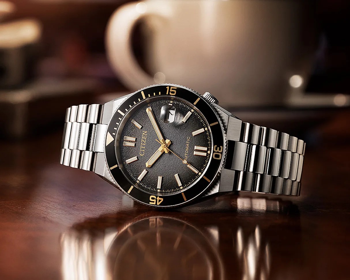 Silver metal Citizen wristwatch with black textured dial and gold-tone markers on a wooden surface.