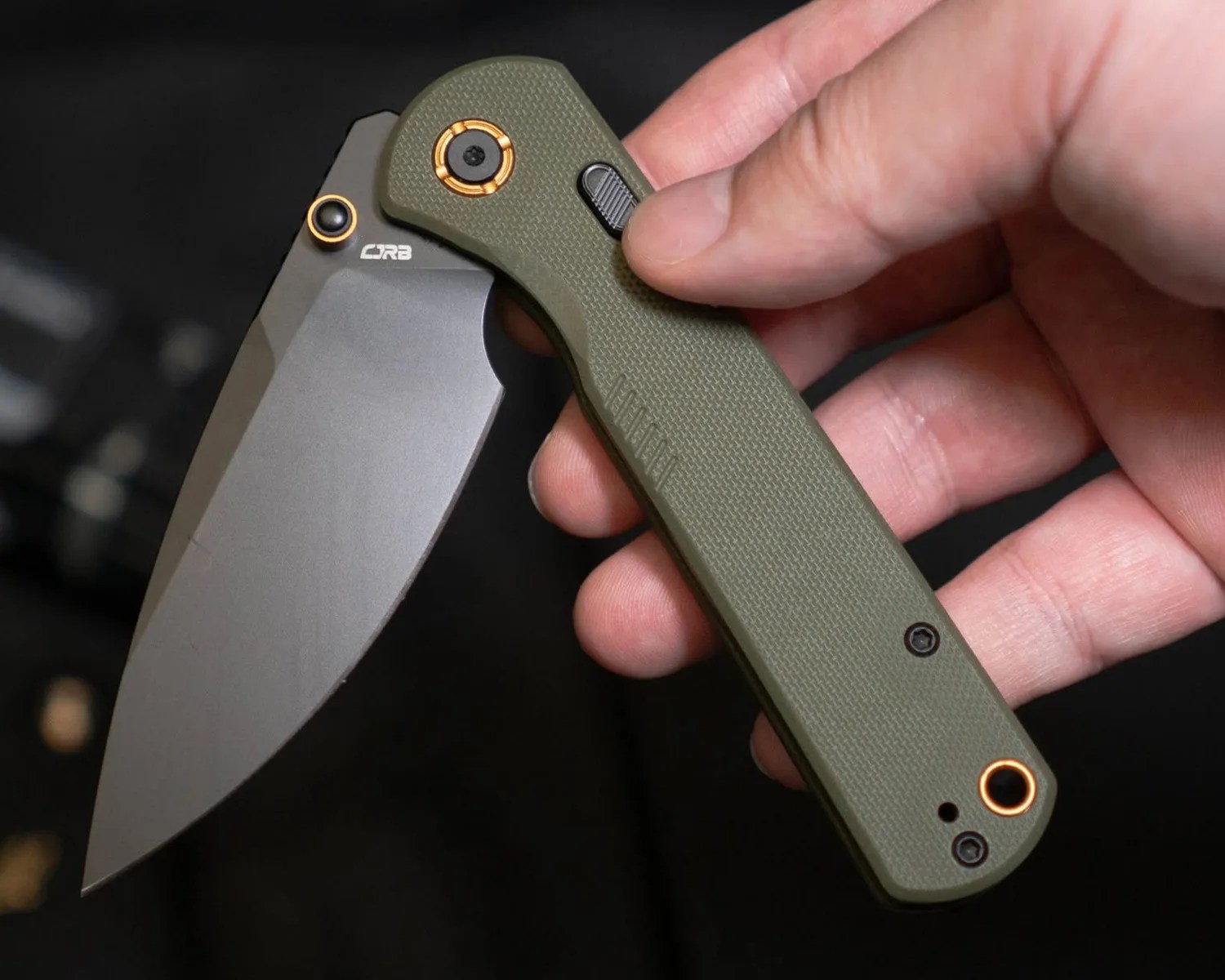 Folding knife with olive green textured handle and gray blade held in a hand.