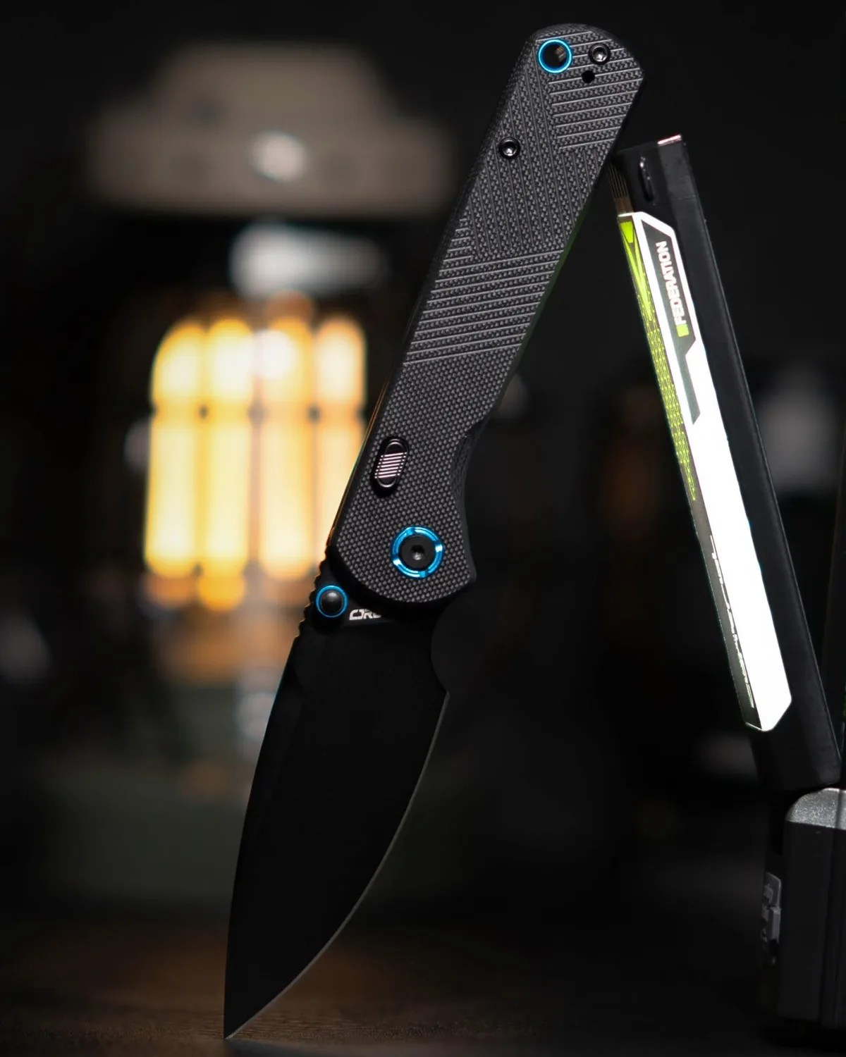 Black folding knife with textured handle and blue accents standing open on a dark surface.