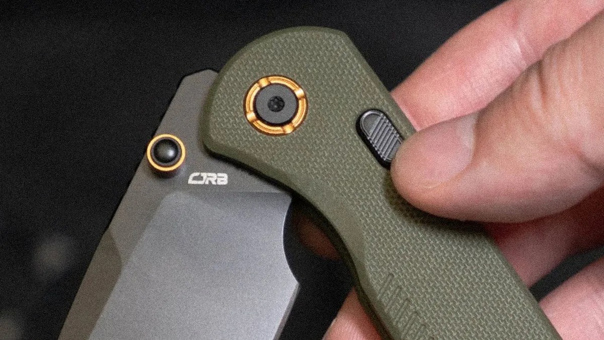 Close-up of a hand holding an olive green folding knife with a black blade marked "CRB" and gold accents.