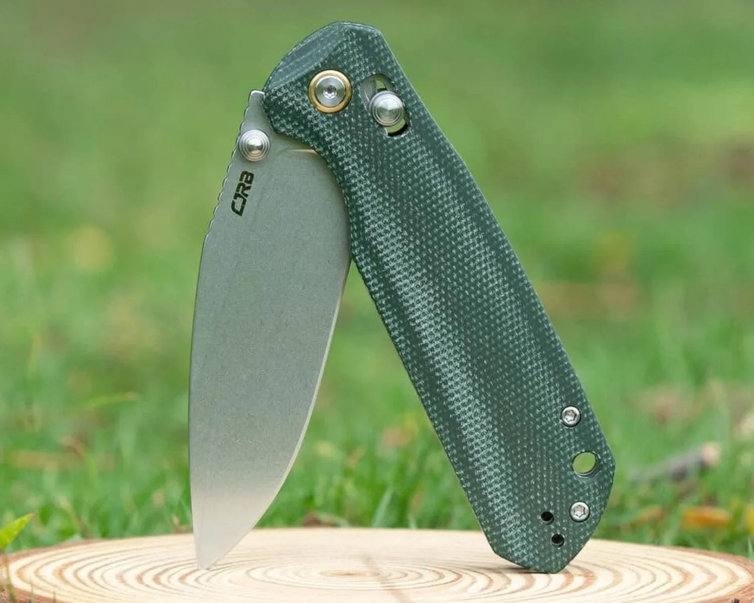 Folding knife with a stonewashed blade and textured dark green handle standing open on a wooden surface.