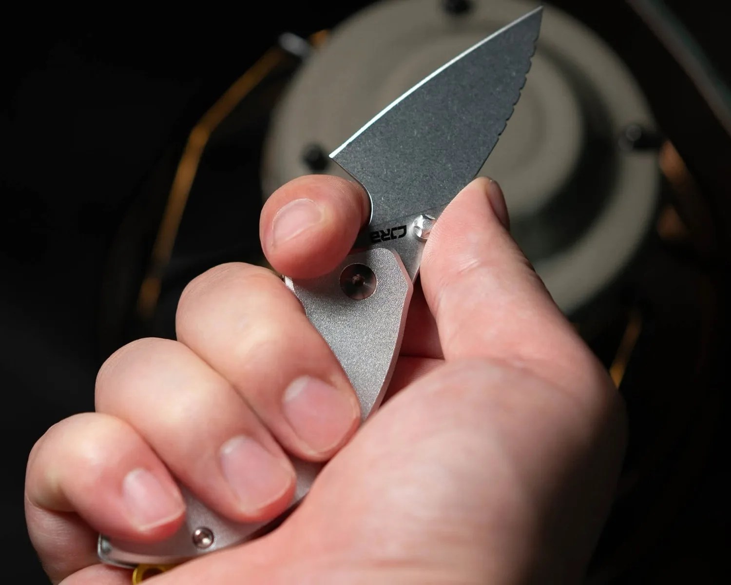 Hand holding a small silver folding knife with a partially serrated blade.