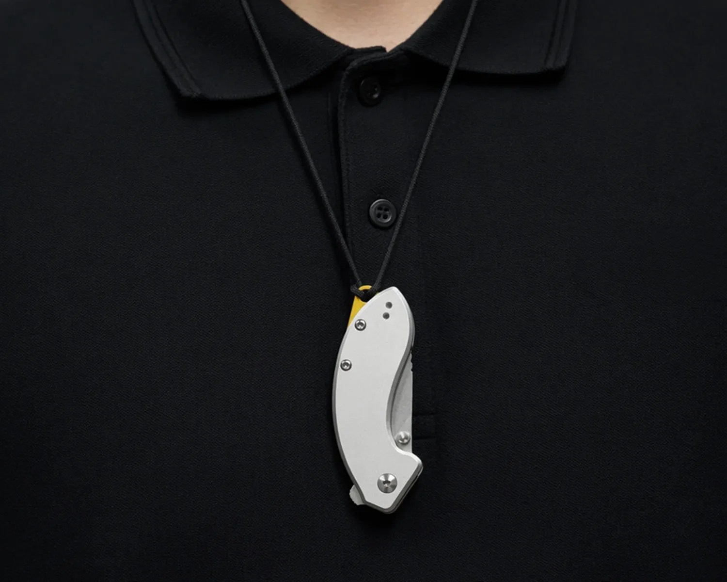 Silver folding knife pendant on a black cord worn over a black collared shirt.