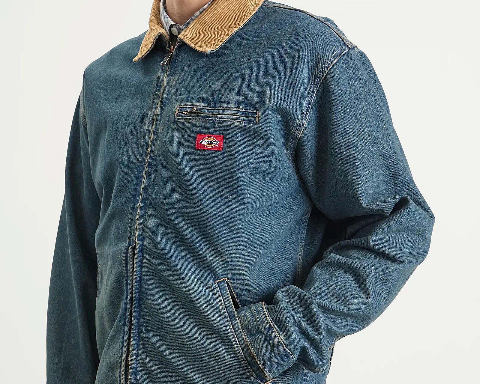 Blue denim jacket with tan corduroy collar and zippered chest pocket worn by a person.