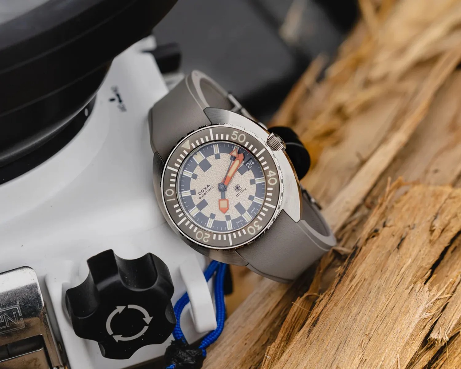 Silver Doxa Army automatic watch with gray bezel and strap resting on wooden surface and white equipment.